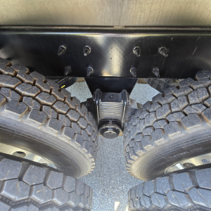 Mack PI64 truck undercarriage showing tandem rear axles with large off-road tires and center suspension component.