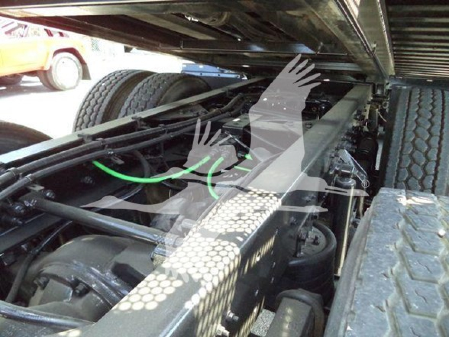Trucks chassis underside view showing heavy-duty suspension and frame near rear wheels; green hoses and mechanical components visible under the cab.
