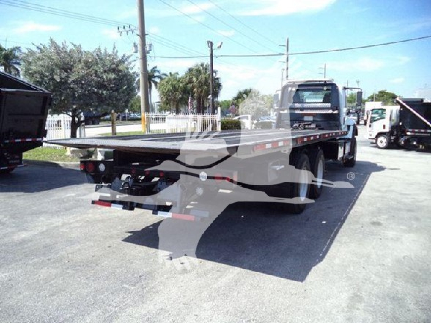 Flatbed tow truck with a long flatbed on a rollback trailer in a lot; back of cab visible; no legible labels or stickers discernible on the image.
