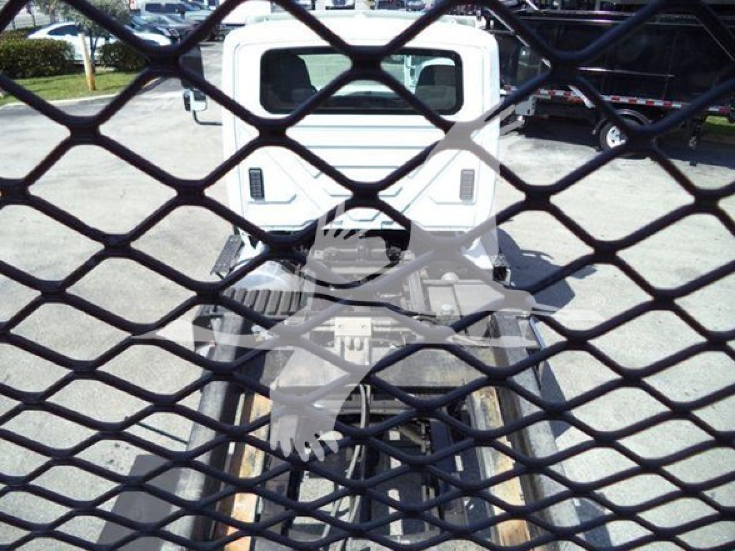 Truck cab rear view through a metal grid fence with equipment behind, showing a white International Workstar 7600 rollback vehicle.