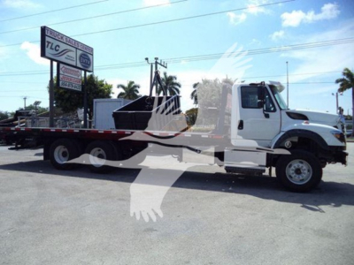 Flatbed tow truck with white cab and long black flatbed showing in-service chassis.