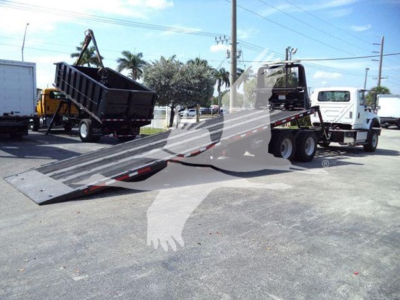 2016 International Workstar 7600 rollback tow truck with long metal ramp extended, dual rear axles, and white cab. Text visible on signs and equipment includes no legible serials. 
