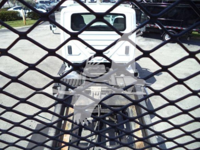Truck cab rear view through a metal grid fence with equipment behind, showing a white International Workstar 7600 rollback vehicle.