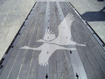 Tractor-trailer flatbed area of a rollback truck showing a wooden deck with metal strips and a watermark of two wings in the center.