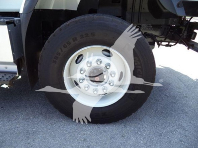 Wheel of truck showing tire with markings and rim bolts; partial chassis visible.