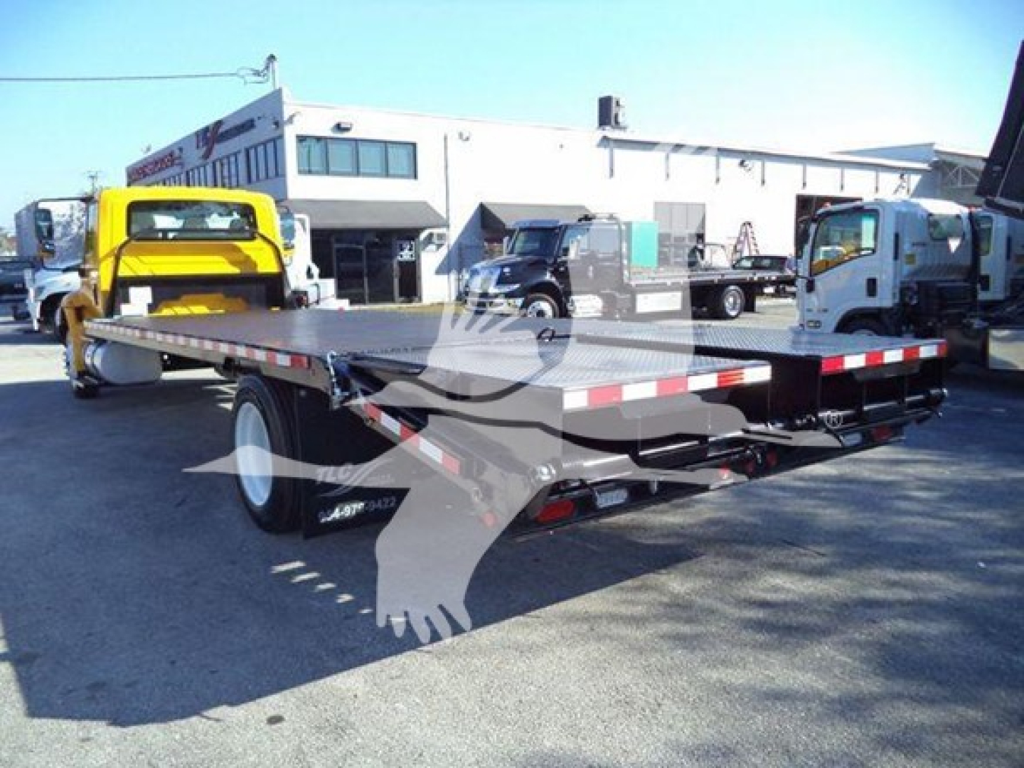 Flatbed tow truck or car hauler trailer in yard with trucks; no visible labels readable.