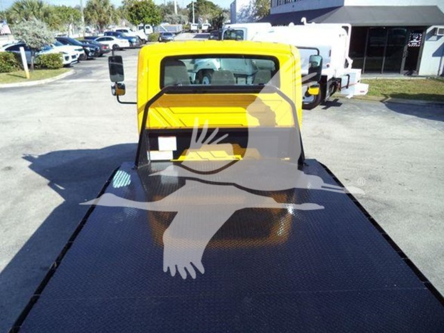 Rear view of a yellow International 4300 auto carrier with a flatbed in a truck lot; visible VIN 3HAMMMML6KL383445 and stock number T83445 in the background.