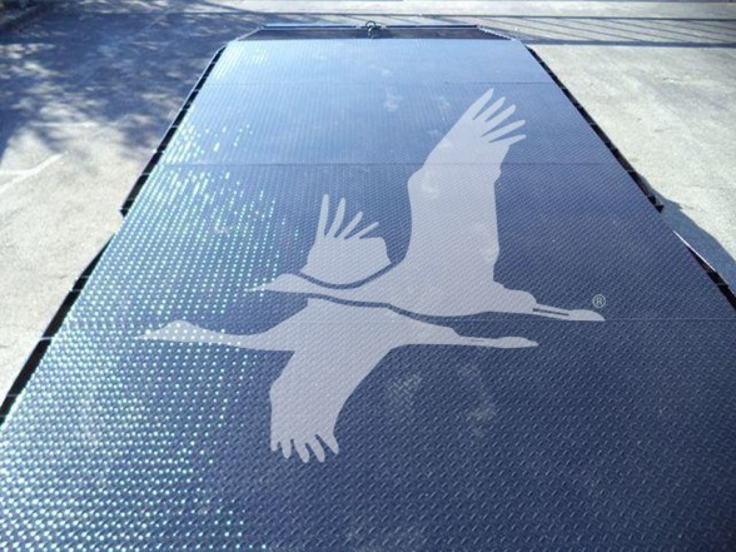 Flatbed truck deck with a large white crane logo in flight, metallic surface with dotted grip pattern along edges.