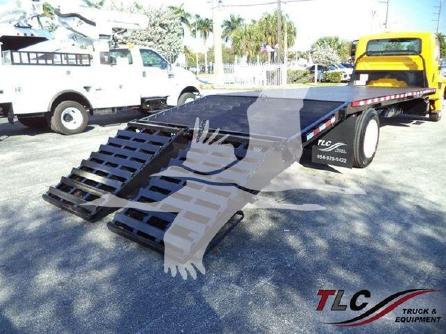 Flatbed tow truck trailer with foldable ramps in an outdoor lot, International 4300 listing, stock number T83445, TLC logo on trailer rail.