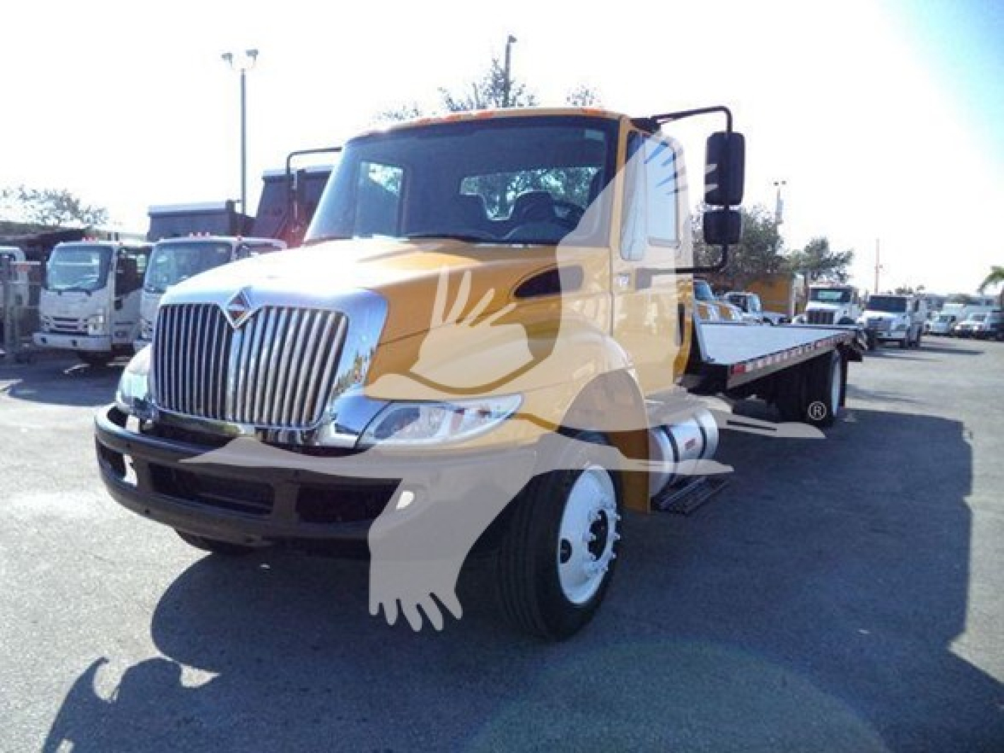 International 4300 tow truck in yellow and white with flatbed, front grille, headlights visible.