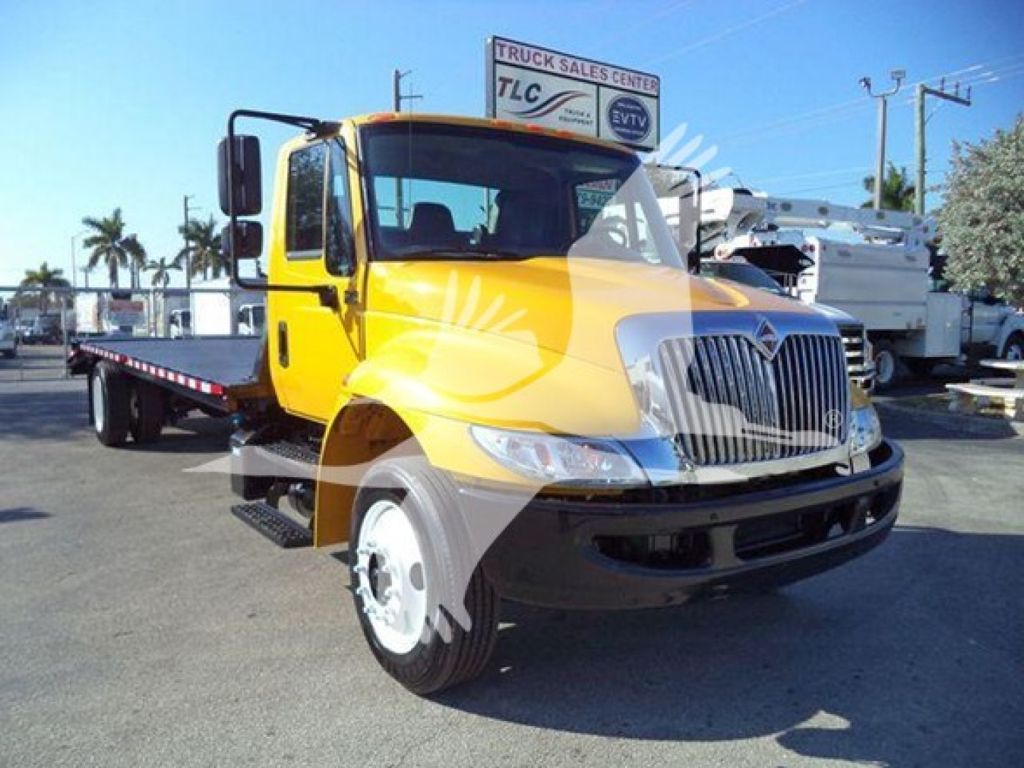 Tow truck with a yellow cab and flatbed, front view, International 4300 model, visible chrome grille and black bumper.
