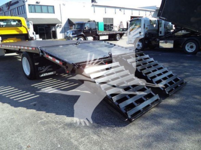 Flatbed tow truck carrier with dual-folding ramps and metallic surface, International 4300 in background.