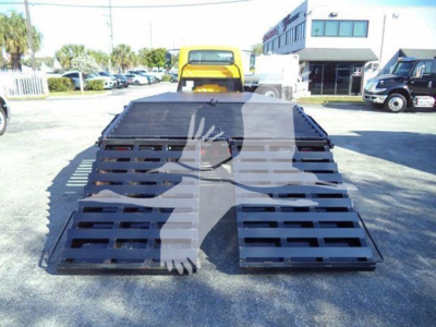 Truck equipment image showing a folded flatbed carrier with a yellow cab behind; no legible brand text visible.