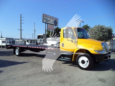 2019 International 4300 auto carrier low cab with flatbed trailer and yellow cab. Visible text on sign reads TLC Trucks, Truck Sales Center. The image shows a yellow International 4300 tow/trailer truck in a dealership lot.