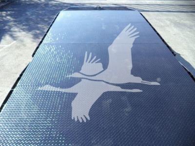 Flatbed truck deck with a large white crane logo in flight, metallic surface with dotted grip pattern along edges.