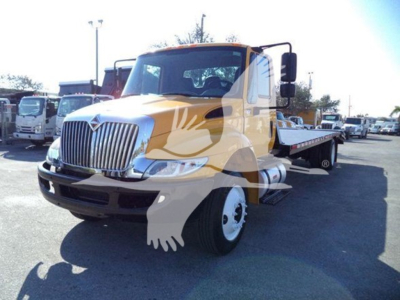 International 4300 tow truck in yellow and white with flatbed, front grille, headlights visible.