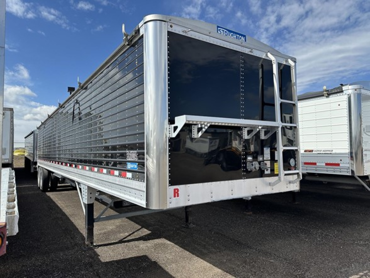Stoughton air ride grain trailer in side/front angle showing polished aluminum sides and open front hopper with hitch and support legs.