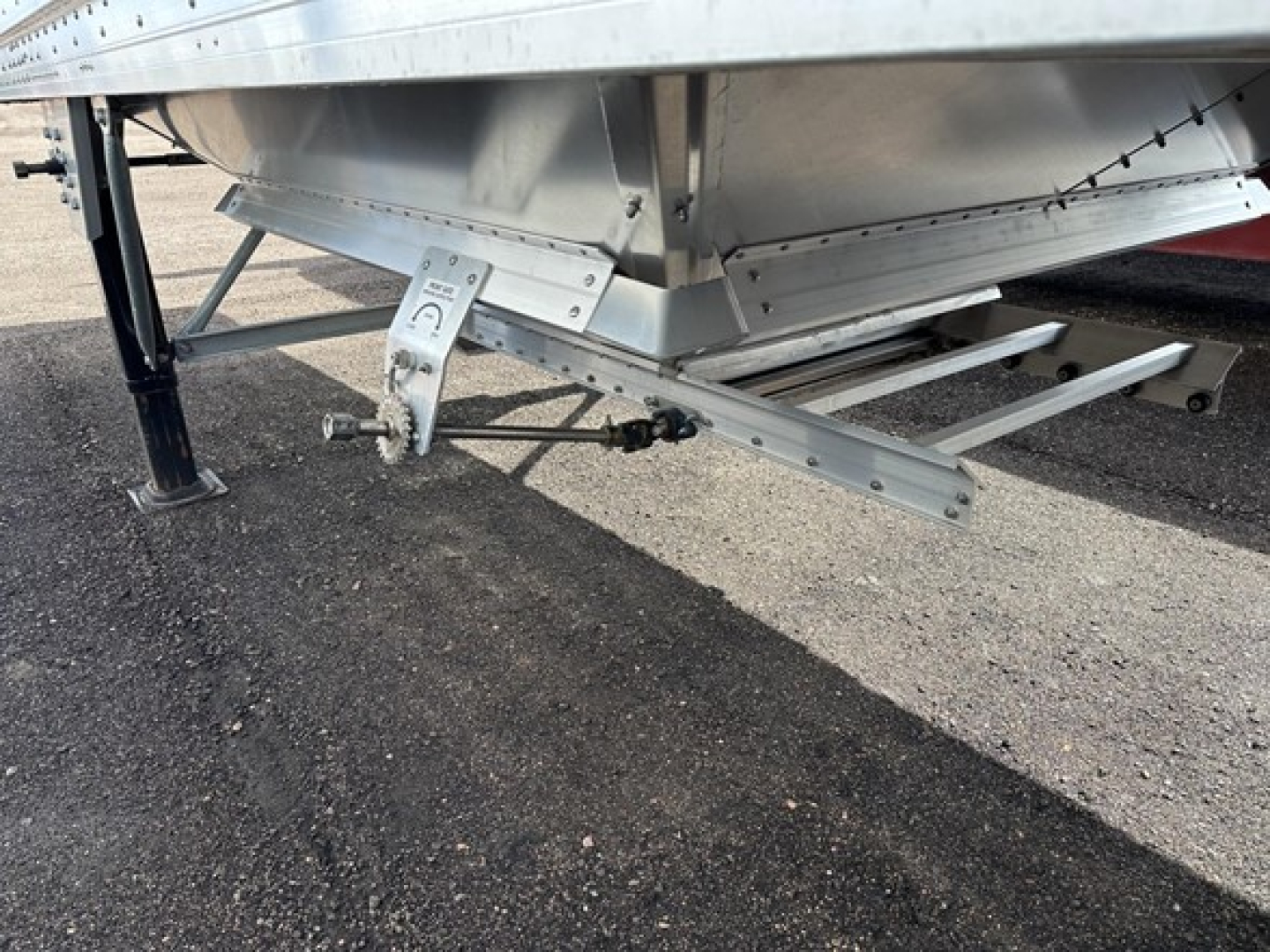 Trailer underside showing support legs and I-beam hitch with labels and hardware; aluminum hopper with riveted joints and stamped components visible.