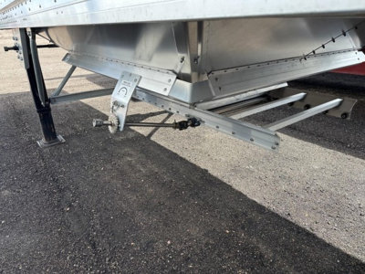 Trailer underside showing support legs and I-beam hitch with labels and hardware; aluminum hopper with riveted joints and stamped components visible.