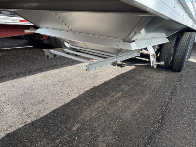 Grain trailer underside view showing suspension and support beams with metal hopper and wheels visible.