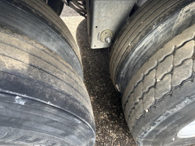 Trailer wheel assembly with dual tires and suspension member in view; tread patterns visible on tires.