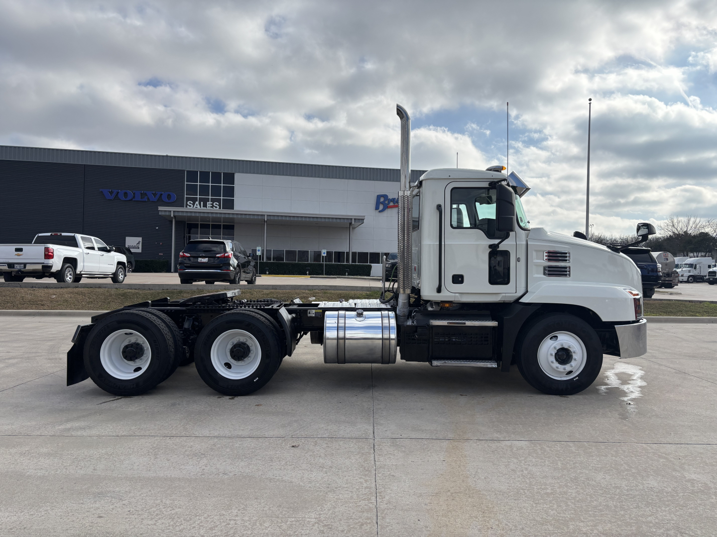 Mack AN64T truck side view showing white cab and chassis with dual rear axles in a dealership lot.