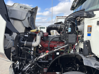 Truck engine bay of a 2020 Mack AN64T; visible components include red engine block, intake hoses, wiring harnesses, and surrounding bay with side panels.