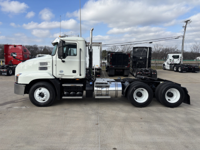 Mack AN64T truck chassis in side profile with sleeper cab, fuel tank, and dual rear axles in a truck lot.