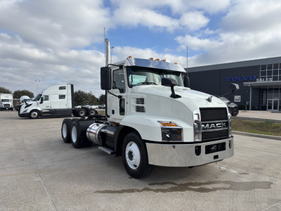 Mack AN64T conventional daycab truck in a dealership lot, white cab with chrome bumper and dual rear axles, Volvo Trucks dealership in background.
