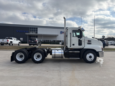 Mack AN64T truck side view showing white cab and chassis with dual rear axles in a dealership lot.