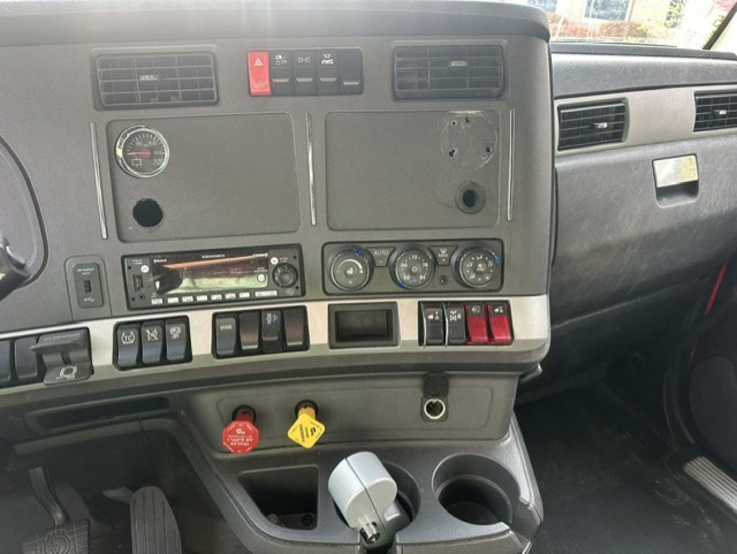 Kenworth T680 cockpit dashboard showing controls, gauges, vents, and cup holders.