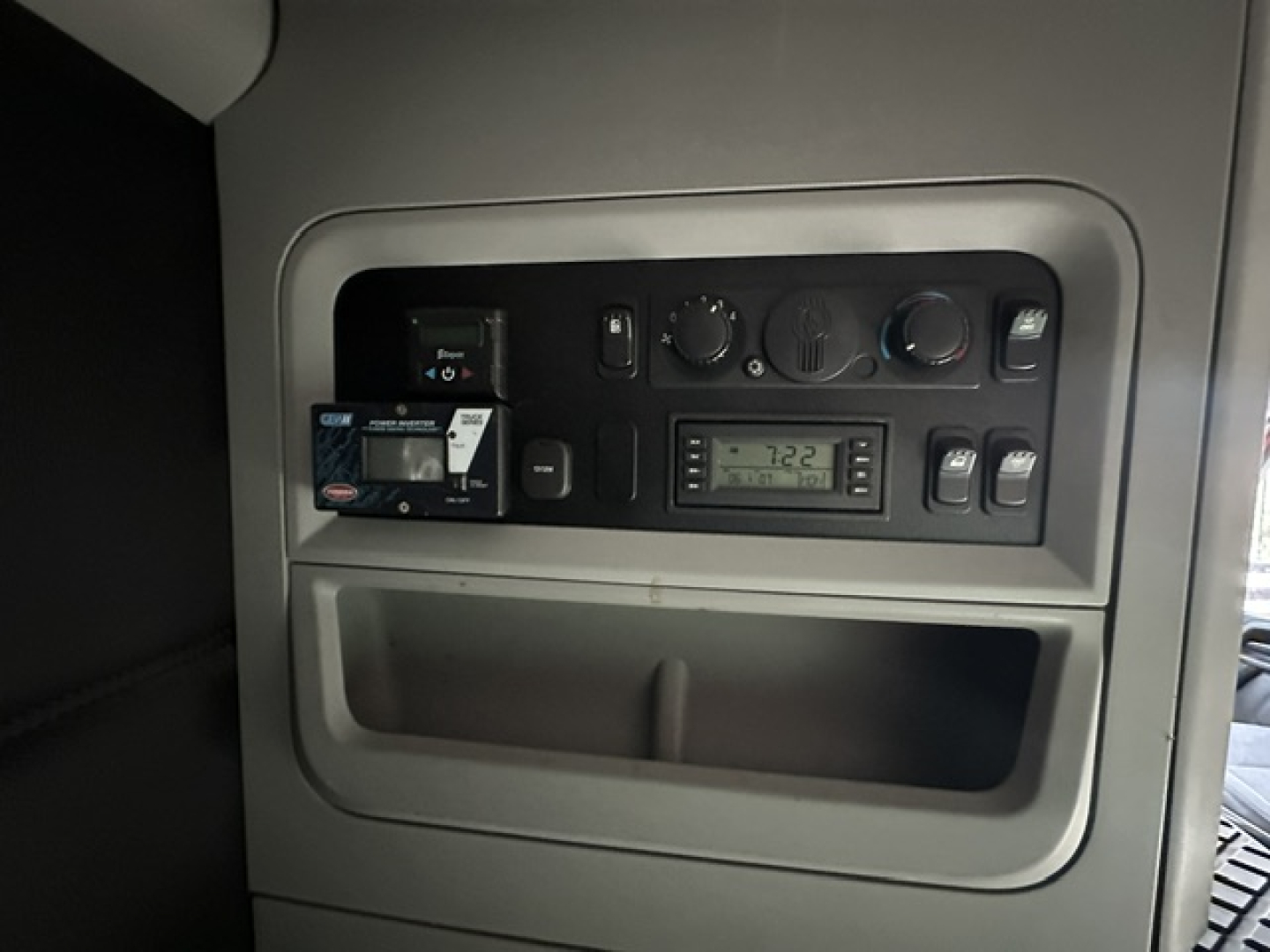 Kenworth T680 cab interior dashboard panel with various gauges and a digital display, small card reader, and control knobs