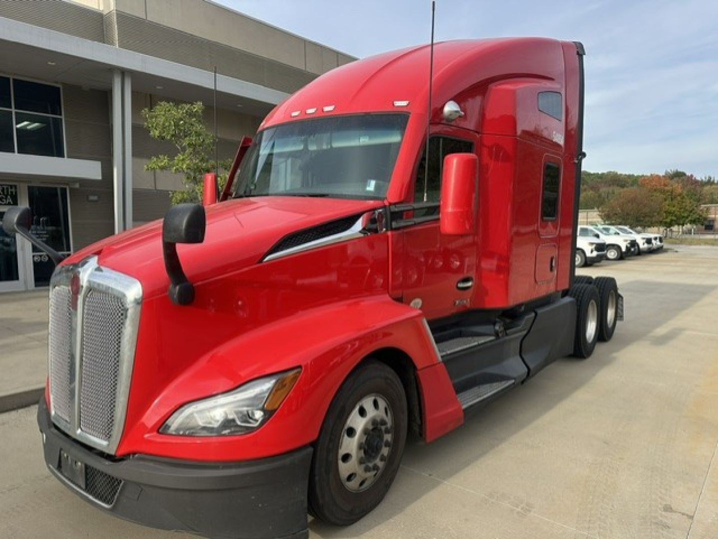 Kenworth T680 tractor in red, front-left view showing large chrome grille, sleeper cab, dual rear axles, and daytime running lights.