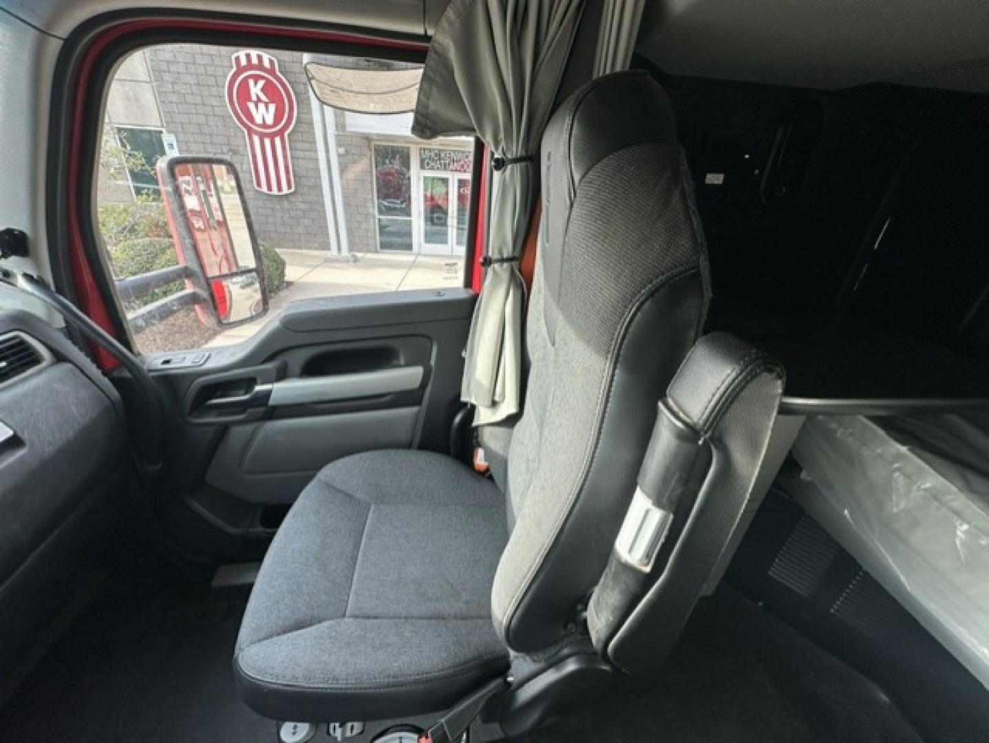 Kenworth truck interior cabin seat and door panel. Visible text includes KW logo outside window. No engine or fluids labeled in image.