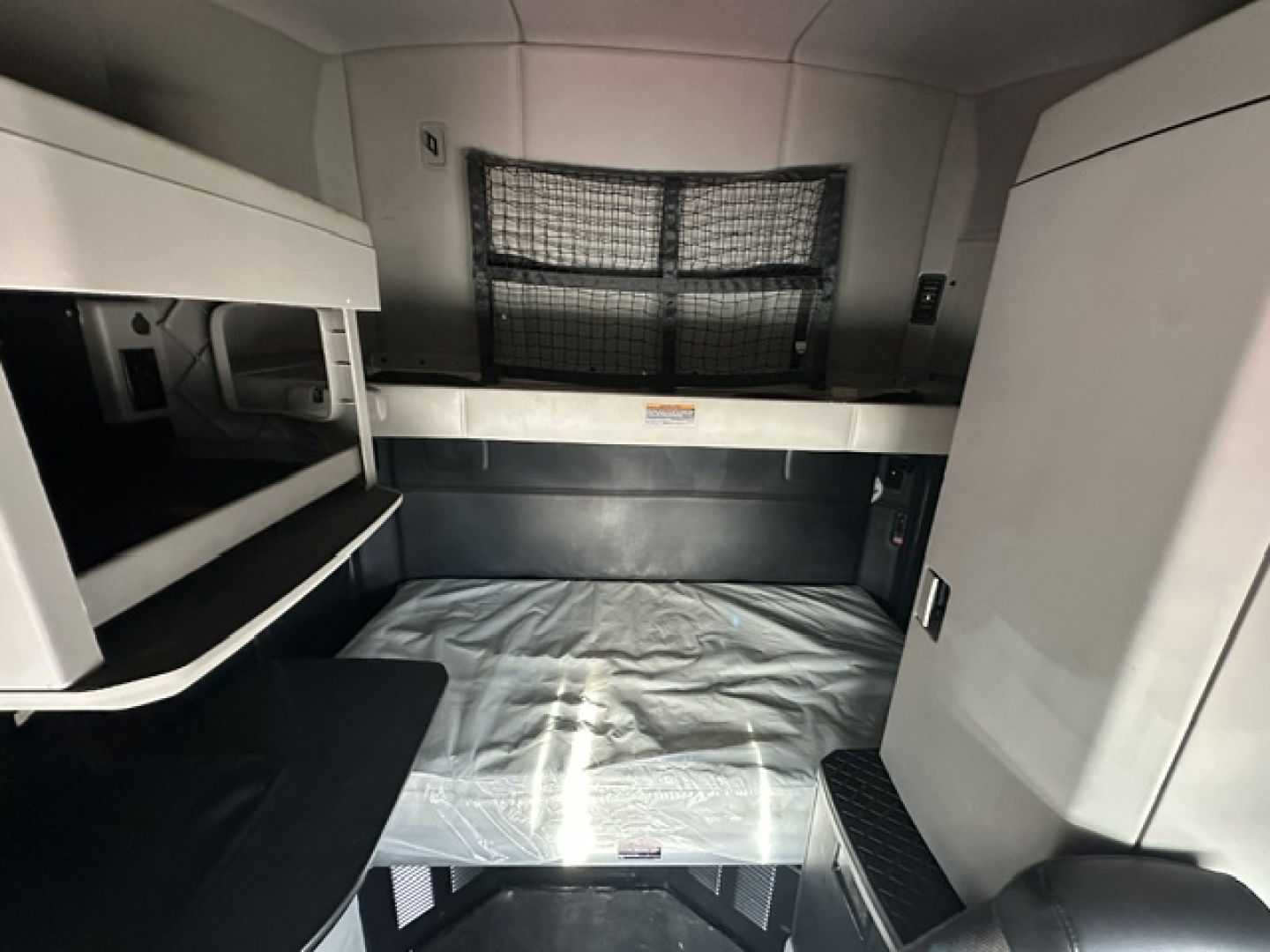 Kenworth T680 sleeper cab interior showing bunk bed area with mattress, side storage, and overhead cabinets.