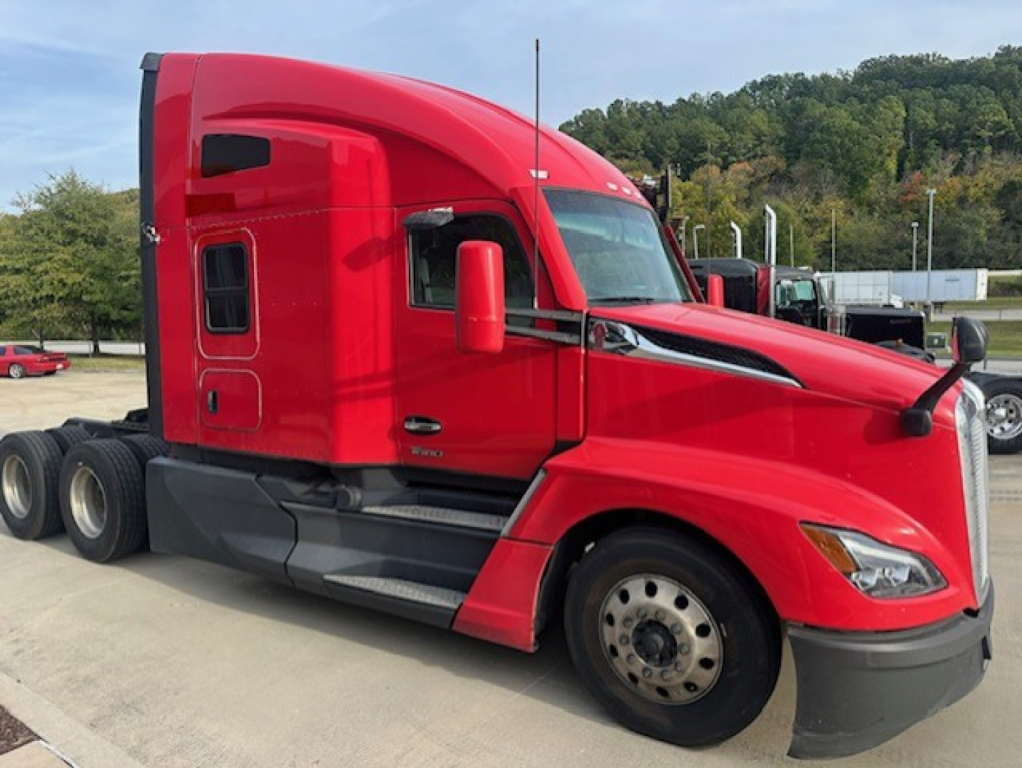 Kenworth T680 tractor-trailer truck in red, side view showing cab interior window and door, with front bumper, wheel, and fender.