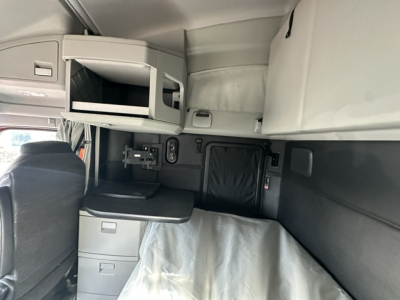Interior of a 2023 Kenworth T680 sleeper cab showing overhead storage, dash controls, and a folded table; no engine or fluid labels visible.