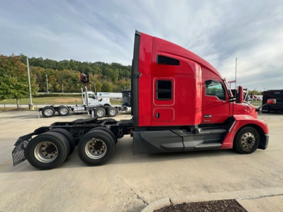 Kenworth T680 tractor side view showing red cab and chassis with triple rear axles and fuel tanks near the cab.