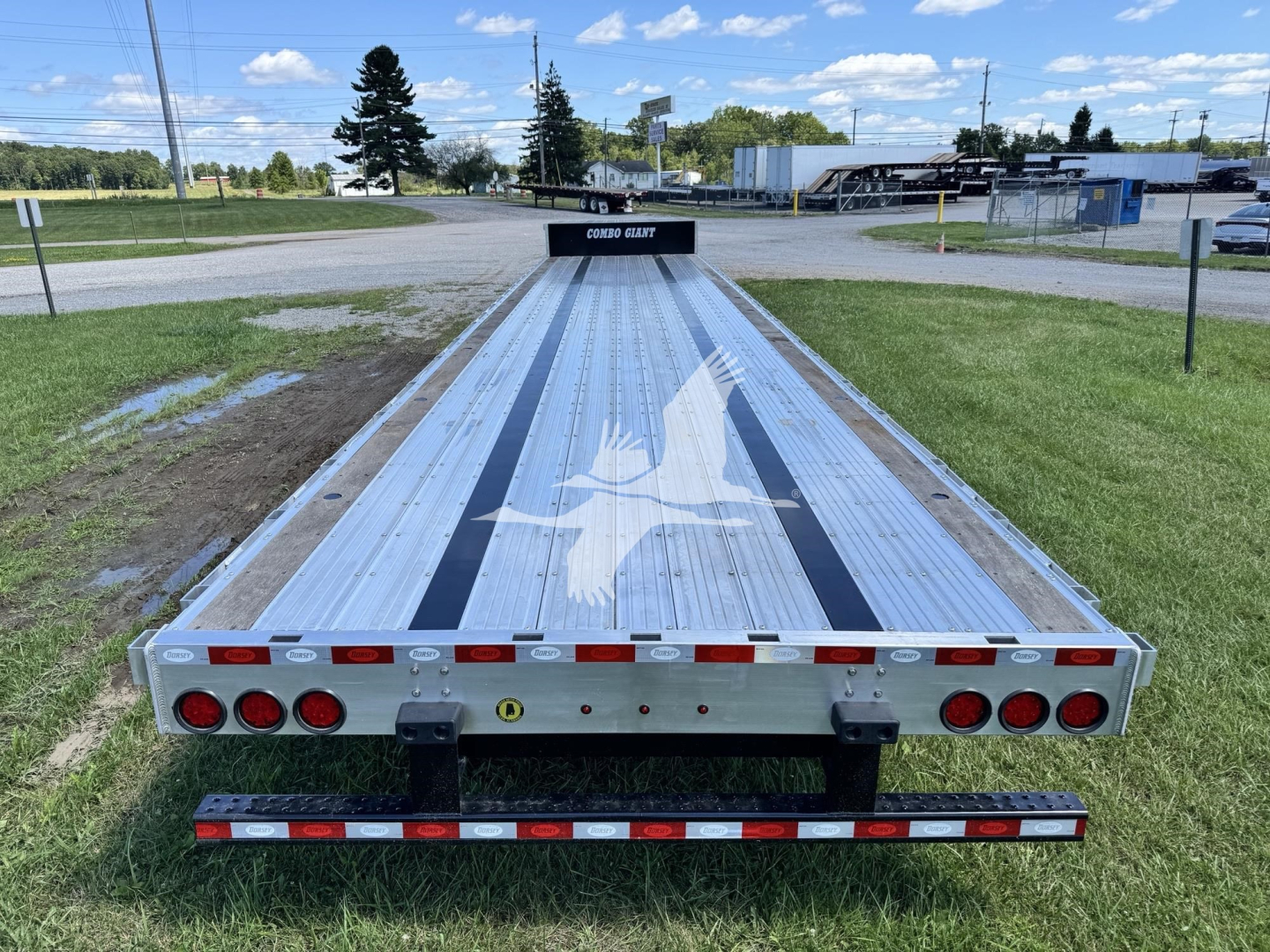 Flatbed trailer from rear showing Dorsey logo on platform, multiple red taillights, reflective tape, and a wheel chock. Visible text: no explicit model beyond the brand on plate and star graphic on deck.