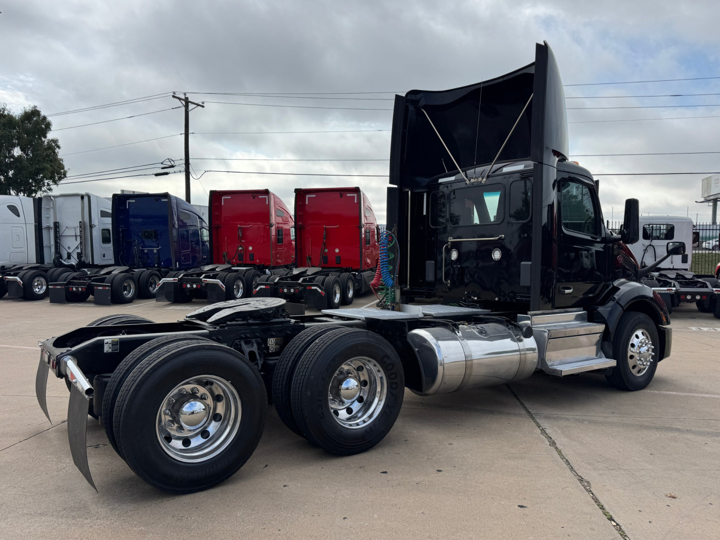 Peterbilt 579 day cab truck chassis and cab with dual rear axles, fuel tanks, and raised hood in a parking lot with other trucks in background.