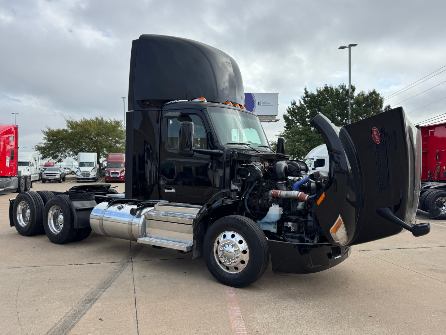 Peterbilt 579 truck in a dealership lot with hood open, showing engine bay and chrome fuel tanks.