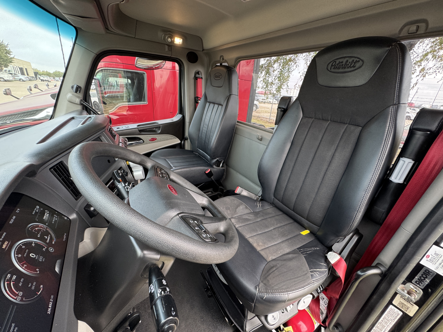 Peterbilt truck interior showing driver's seat and passenger seat with steering wheel, dashboard gauges, and window view; no visible text on components.