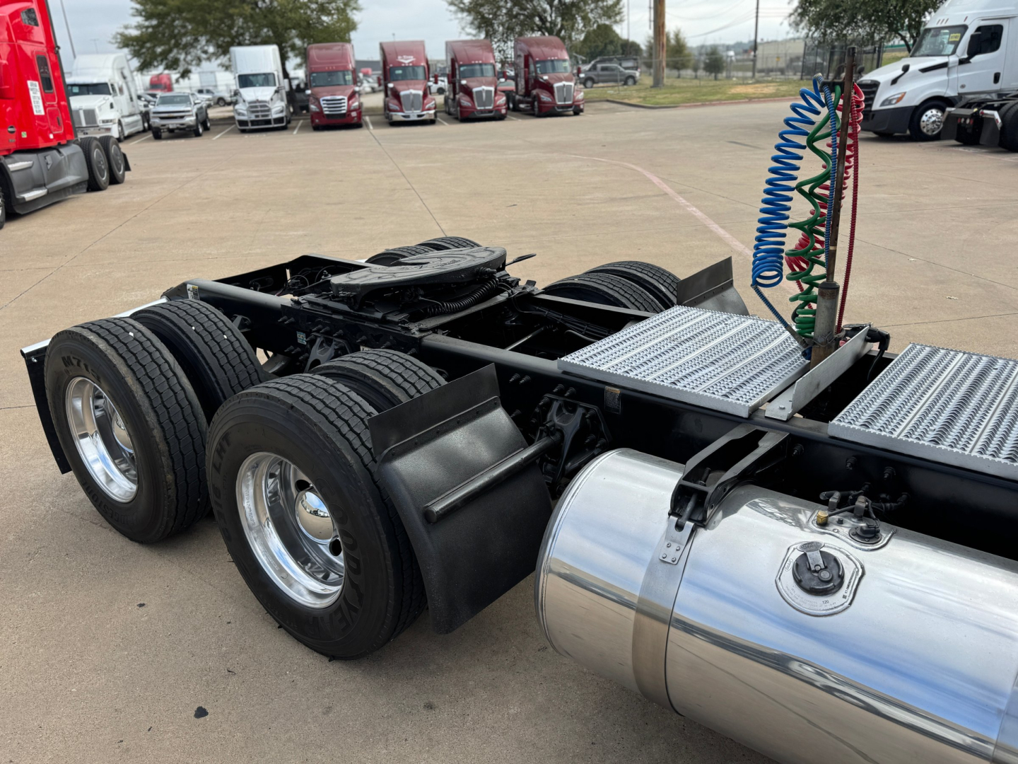 Peterbilt 579 chassis with dual rear axles and chrome fuel tank, cabless area showing air lines and silver fuel tank, part of a used tractor-trailer on lot