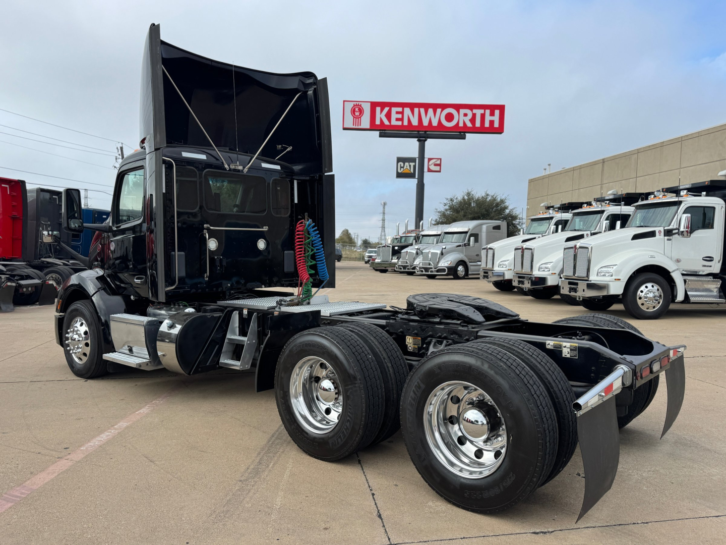 Peterbilt 579 conventional daycab tractor chassis with dual rear axles and empty sleeper area, showing front of cab with open fifth wheel, chrome wheels, and Kenworth sign in background.