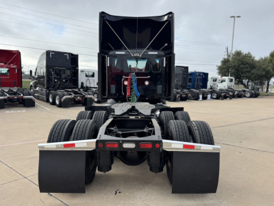 Peterbilt cab and chassis rear view showing dual rear axles and mudflaps with fifth wheel area; show truck bed and stacked trucks in background.