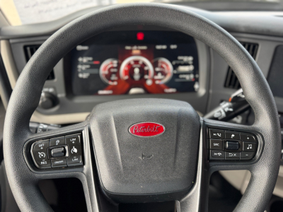 Peterbilt 579 cabin interior with steering wheel and digital gauge cluster visible, shows Peterbilt logo on wheel center, control buttons on both sides of the wheel