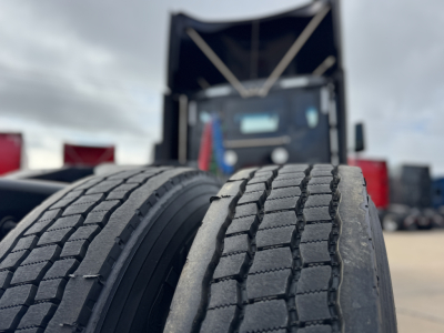 Two front truck tires in foreground with a Peterbilt 579 truck in background; no legible labels visible on tires or vehicle from this angle.