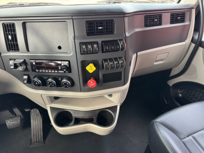 Peterbilt 579 interior dash area showing center console with climate controls, cup holders, and several switches and yellow/red lanyard labels.