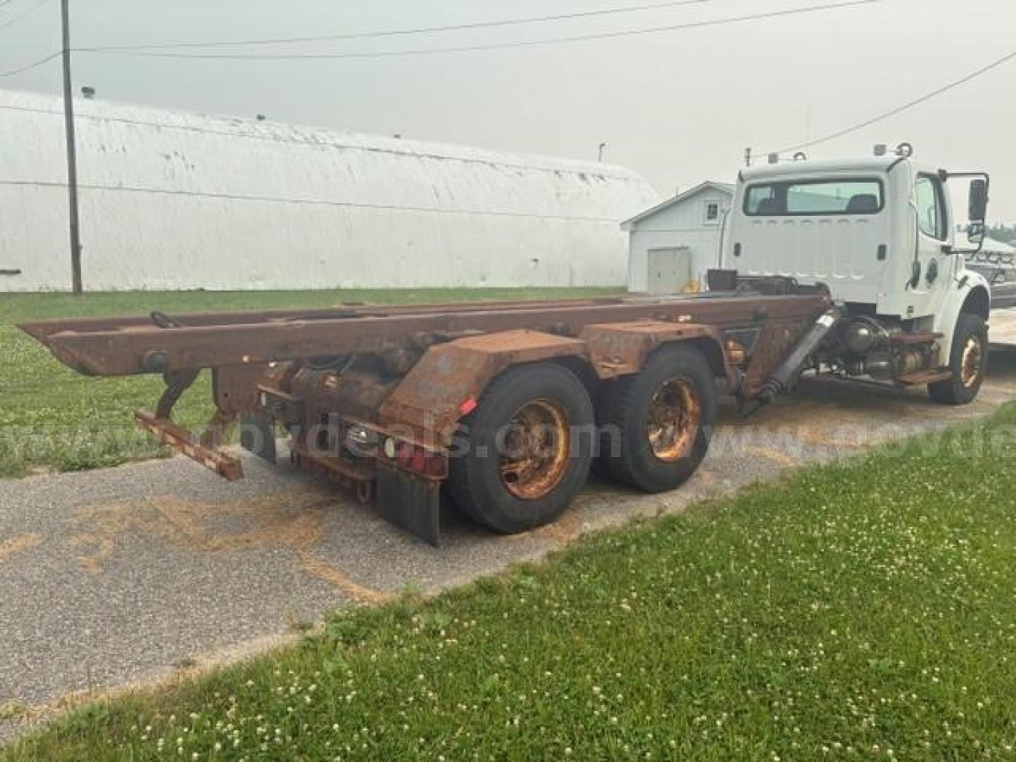 Freightliner M2 106 cab and chassis showing rusty flatbed trailer and white cab