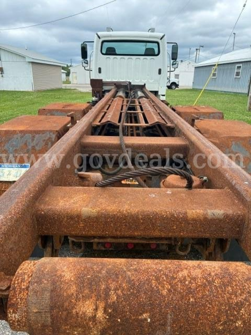 Rear view of a rusty freightliner m2 106 cab and chassis frame showing chassis rails and fifth wheel area.